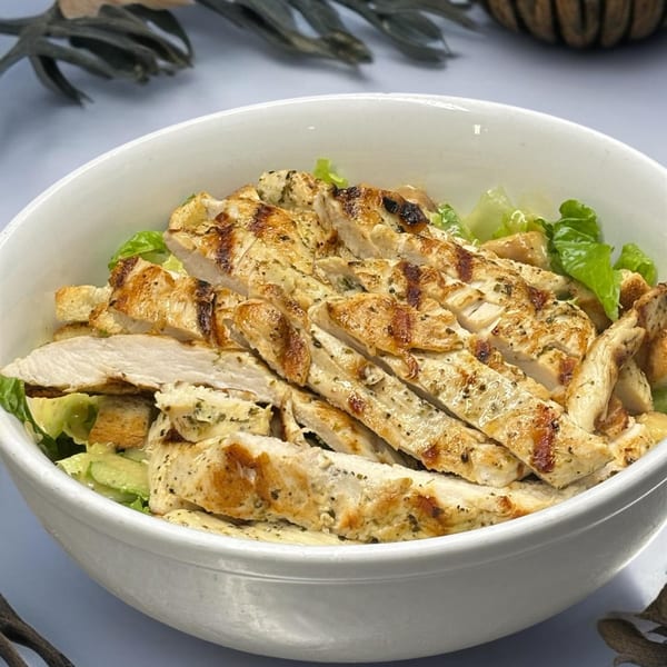 Grilled chicken Caesar salad with croutons and fresh lettuce in a white bowl at Jimmy's Grand Cafe.