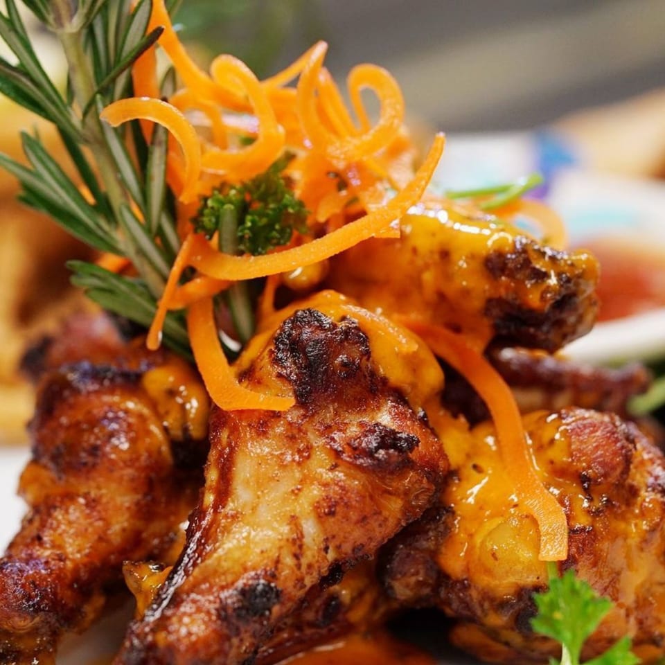 Close-up of Jimmy's Grand Cafe's glazed chicken wings, garnished with rosemary and carrot curls.