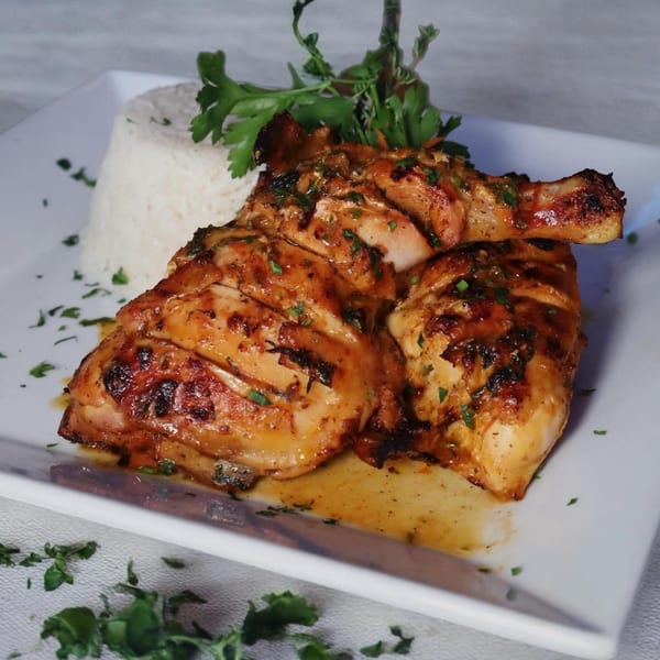 Grilled chicken with herbs and spices, served with a side of white rice and garnished with parsley.