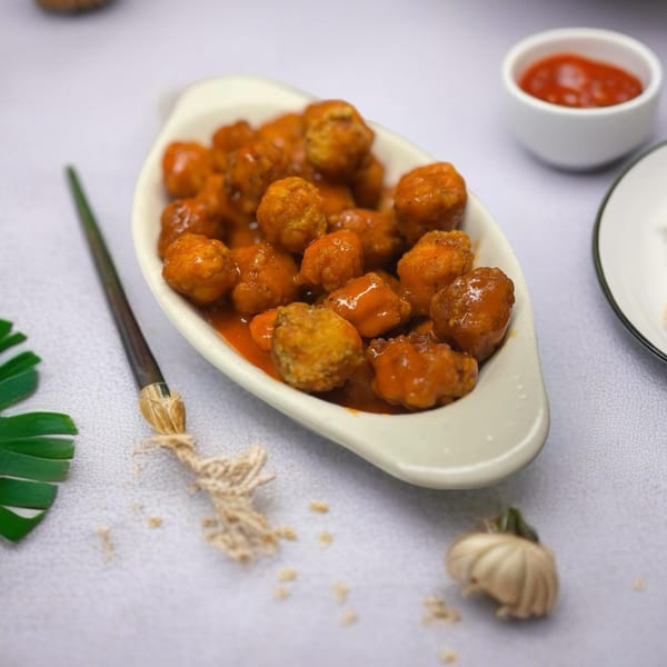 A white boat-shaped dish filled with orange-glazed meatballs, with a small bowl of sauce nearby.
