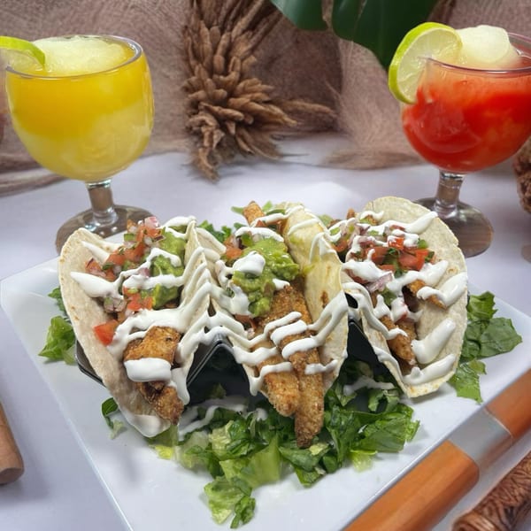 Three fish tacos with guacamole, pico de gallo, and crema, served with two frozen margaritas.