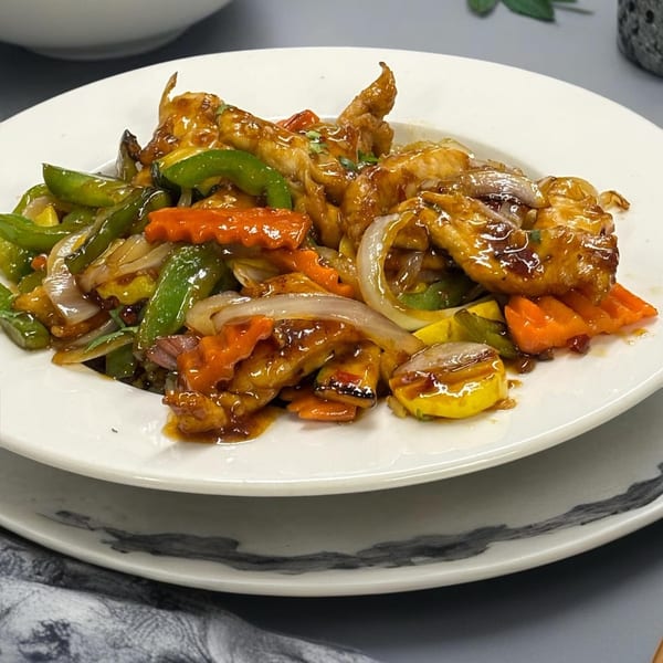 Sweet and sour chicken with bell peppers, carrots, onions, and squash on a white plate.
