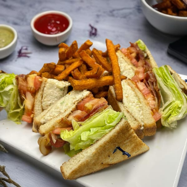 A diner club sandwich with bacon, lettuce, and tomato, served with sweet potato fries and dipping sauces.