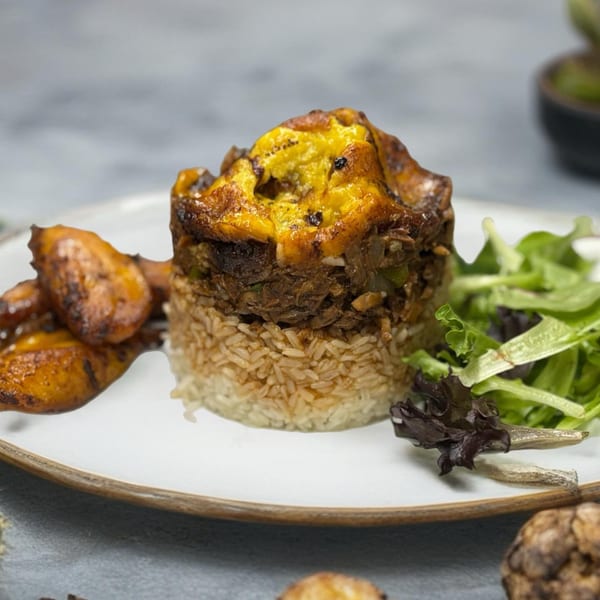 Savory meat and plantain dish over rice, with a side of greens and fried plantains.