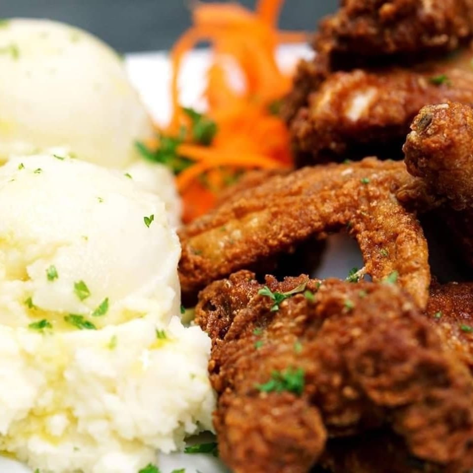 Crispy fried chicken wings with mashed potatoes and shredded carrots, garnished with parsley.