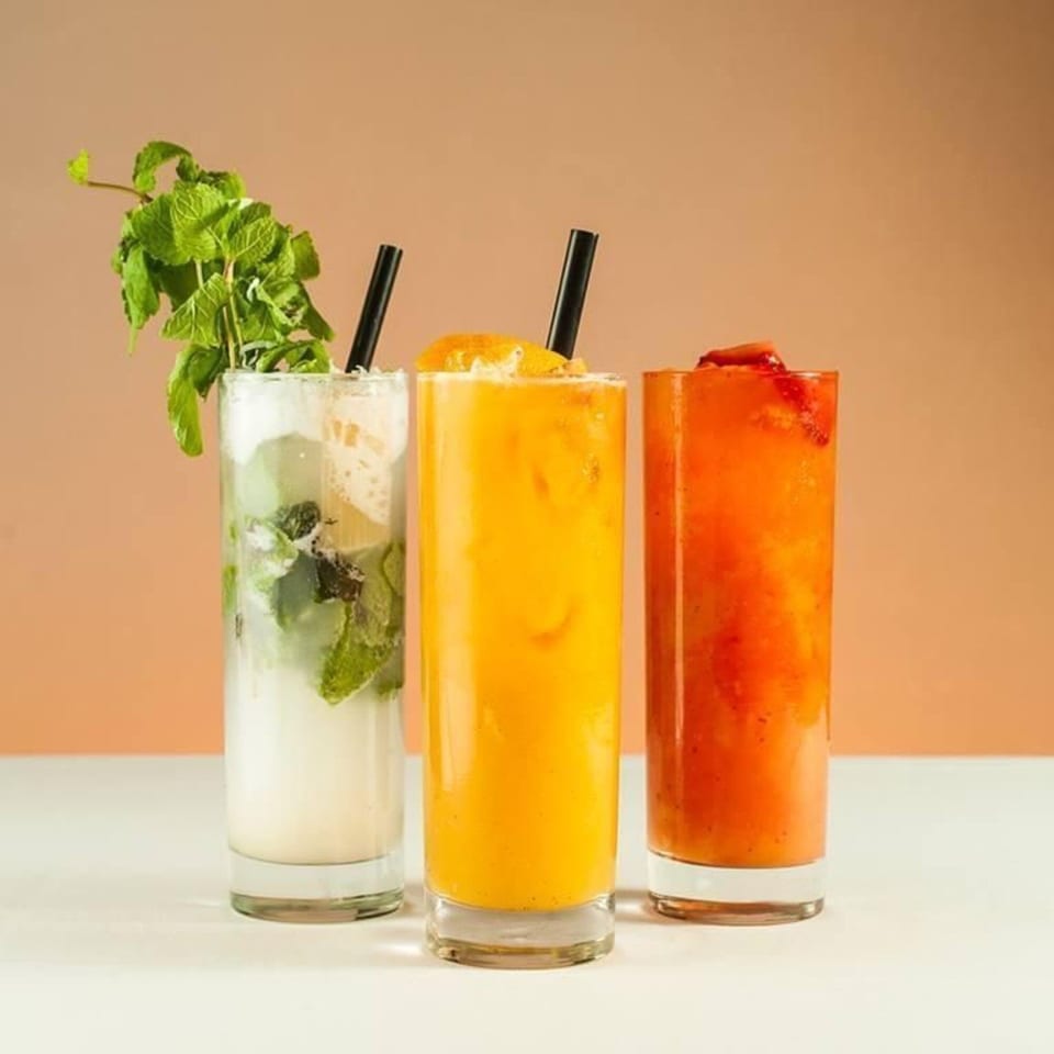 Three tall glasses of colorful drinks: a mojito, an orange juice, and a strawberry smoothie.