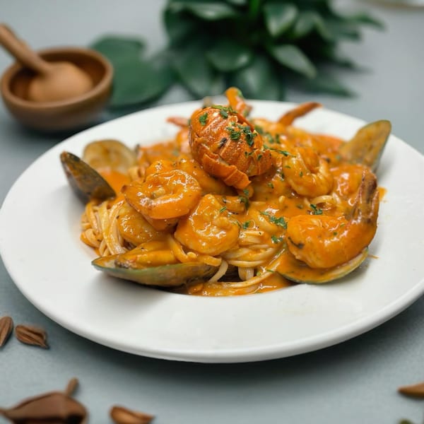 Seafood pasta with shrimp, mussels, and a lobster tail in a creamy orange sauce, garnished with herbs.
