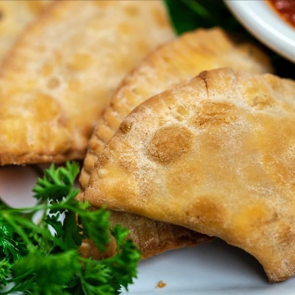 Golden-brown empanadas, garnished with fresh parsley, and a side of red dipping sauce.