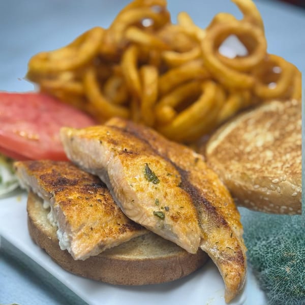 Grilled salmon fillets on toast with curly fries, tomato, and a sesame bun.